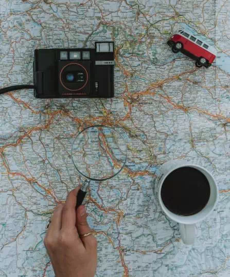 Aparat, zabawka, lupa i kubek z kawą na tle mapy